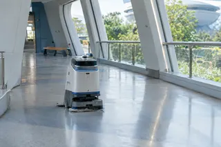 Autonomous cleaning robot navigates a spacious, modern corridor with large windows and polished floors.