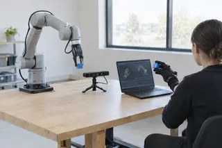 Person uses a glove to control a robotic arm at a desk, with motion data displayed on a laptop and sensor nearby.
