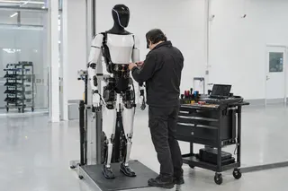 Technician works on a standing humanoid robot in a bright, modern lab with a tool cart nearby.